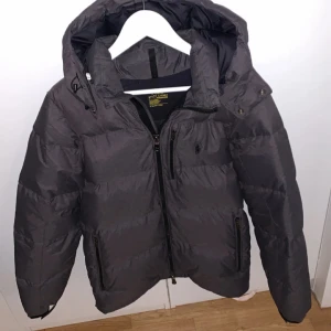 Ralph lauren jacka - Säljer en grå pufferjacka från Ralph lauren i mycket bra skick. Den är perfekt för vintern med sin tjocka vaddering och har en praktisk huva. Jackan har dragkedja och två fickor med dragkedjor. Den är långärmad och passar bra för kalla dagar. Perfekt för dig som vill hålla dig varm och snygg! 🧥