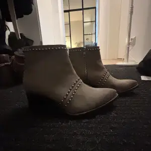 Snygga beige boots från Primeboots i mocka med coola nitar och dragkedja på sidan. De har en spetsig tå och en stabil klack som ger en edgy look. Perfekta för höst och vår när du vill ha något stilrent men med attityd. Passar både till jeans och klänning! Nypris 2000kr 