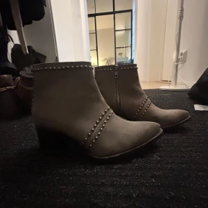 Beige boots med nitar från Primeboots - Snygga beige boots från Primeboots i mocka med coola nitar och dragkedja på sidan. De har en spetsig tå och en stabil klack som ger en edgy look. Perfekta för höst och vår när du vill ha något stilrent men med attityd. Passar både till jeans och klänning! Nypris 2000kr 