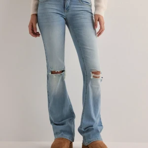 Ljusblå bootcut jeans med slitningar - Säljer ett par snygga ljusblå bootcut jeans med coola slitningar på knäna. Perfekta för en avslappnad stil och passar både till vardags och fest. De har en klassisk femficksdesign och är superbekväma att bära. Perfekta för vår och sommar!