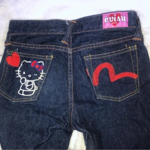 Evisu jeans med Hello Kitty-motiv - Säljer ett par rare Evisu jeans med Hello Kitty-motiv på bakfickan. De är mörkblå med röda detaljer och har en söt röd hjärta bredvid Hello Kitty 🐱❤️
