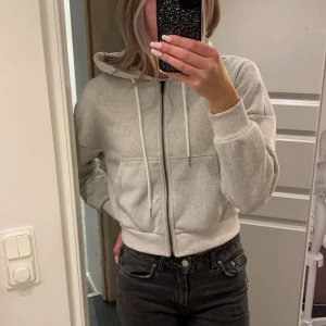 Grå hoodie med dragkedja - Säljer en grå hoodie som är lite kortare! Aldrig använd 