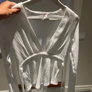 Vit ribbad omlottopp - Säljer en superfin vit ribbad omlottopp med långa ärmar. Toppen har en v-ringad design och knytning i midjan som ger en smickrande passform. Perfekt för både vardag och festliga tillfällen!