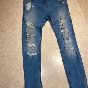 Blå skinny jeans från H&M - Säljer ett par blå skinny jeans från H&M i storlek 34. De har en cool slitningseffekt på framsidan som ger en trendig look. Perfekta för en avslappnad stil. Materialet är 99% bomull och 1% elastan, vilket gör dem bekväma och stretchiga.