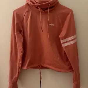 Säljer en snygg rostfärgad hoodie från Stronger. Den har en hög krage och en randig detalj på ena ärmen. Den är i mycket bra skick och superbekväm att ha på sig. Passar perfekt till både träning och chill.