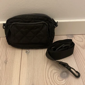 Svart liten axelrems väska i svart! - Säljer en liten svart väska som man får plats med mobilen, plånbok och något litet! Den har även ett justerbar rem som du kan justera längd och ta av och på den från väskan!💕 tror den är köpt på Kappahl men är inte säker på priset! Den är i gott skick!