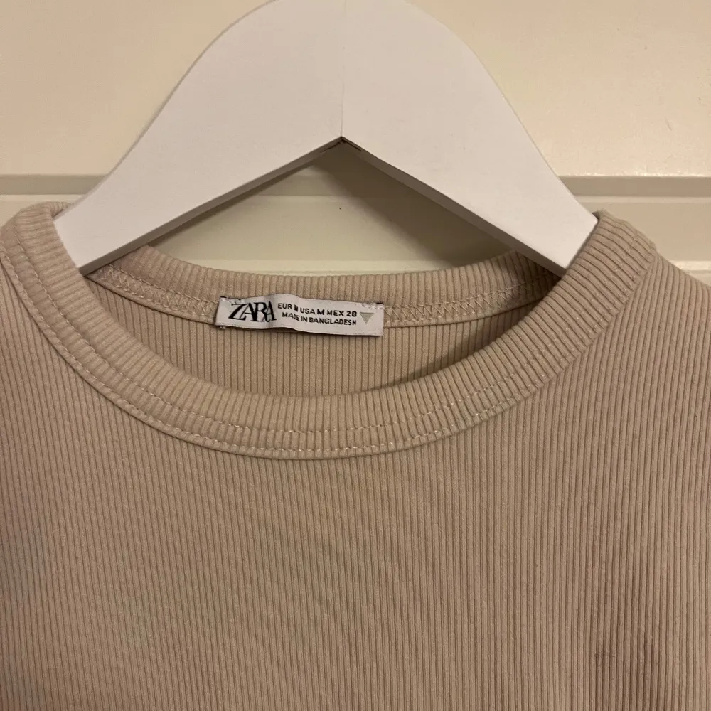 Säljer en superfin beige ribbad T-shirt från Zara i storlek XS. Den har en tight passform och korta ärmar. Toppar.