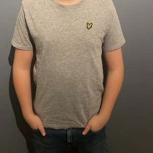 Grå t-shirt med broderad logga - Säljer en stilren grå t-shirt från Lyle & Scott i mycket bra skick. Den har en broderad gul logga på bröstet och är kortärmad. Perfekt för vardagsbruk eller en avslappnad dag ute. Passar bra till jeans eller shorts! PRISET ÄR EJ SKRIVET I STEN!!!