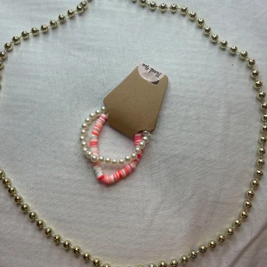  armband i pärlor - Säljer ett set med  två Armband. Armbanden är elastiska, ett med vita pärlor och ett med rosa och vita runda pärlor. Perfekt för att piffa upp en outfit till fest eller vardag!