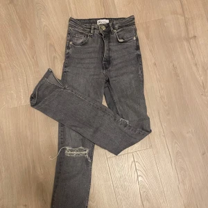 Grå jeans med slitningar - Säljer ett par grå jeans från Zara i bra skick. De är ganska smala upptill sen bootcut där nere och slitningar vid knäna. Sitter smickrande