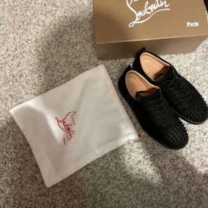 Svarta loubitins  - Säljer ett par svarta Louboutin sneakers i mycket bra skick. De har en cool design med nitar på ovansidan och den ikoniska röda sulan. Perfekta för att ge din outfit en edgy touch. Skorna kommer med originalförpackning och dustbag. Saknas en spik men det märks inte ens milt smutsiga för använda fåtal gånger därför är priset lågt 