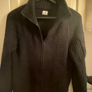  C.P. Company - Säljer en snygg svart stickad tröja från C.P. Company. Den har en dragkedja vid halsen och en cool detalj på ärmen. Perfekt för höst och vinter, håller dig varm och stilren. Passar både till vardags och lite finare tillfällen. Skulle behöva noppras därav priset!🖤