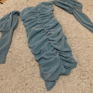 Glittrig blå klänning - Säljer en superfin glittrig blå klänning med rynkade detaljer. Den har långa ärmar och en tight passform som verkligen framhäver figuren. Perfekt för festliga tillfällen! ✨