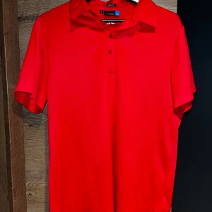 Röd pikétröja från J.Lindeberg - Säljer en snygg röd pikétröja från J.Lindeberg i storlek M. Tröjan har en klassisk krage med knappar och är i regular fit. Perfekt för både vardag och festliga tillfällen. Den är i mycket bra skick och redo för en ny ägare!