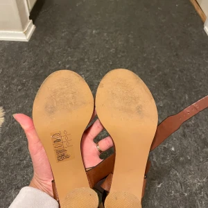 Bruna sandaler med klack från H&M - Snygga bruna sandaler från H&M i bra skick. De har en bekväm klack och justerbara remmar med spänne. Perfekta för sommarens fester eller en dag på stan. Tillverkade i syntetmaterial med en stilren design.