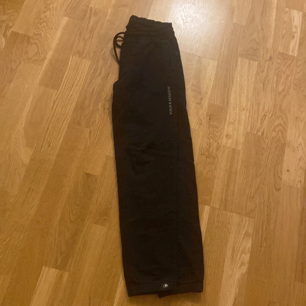 Säljer ett par svarta mjukisbyxor från Scotch & Soda i 152 12 år. Byxorna har en bekväm passform med snörning i midjan och är perfekta för en avslappnad stil. De är i mycket bra skick och passar perfekt för höst och vinter.. Farkut & Housut.