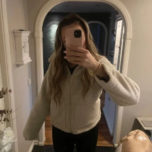 Beige teddyjacka - Mysig beige teddyjacka med dragkedja. Perfekt för kyliga dagar och ger en avslappnad look. Jackan har långa ärmar och en normal passform. Superbekväm och trendig!