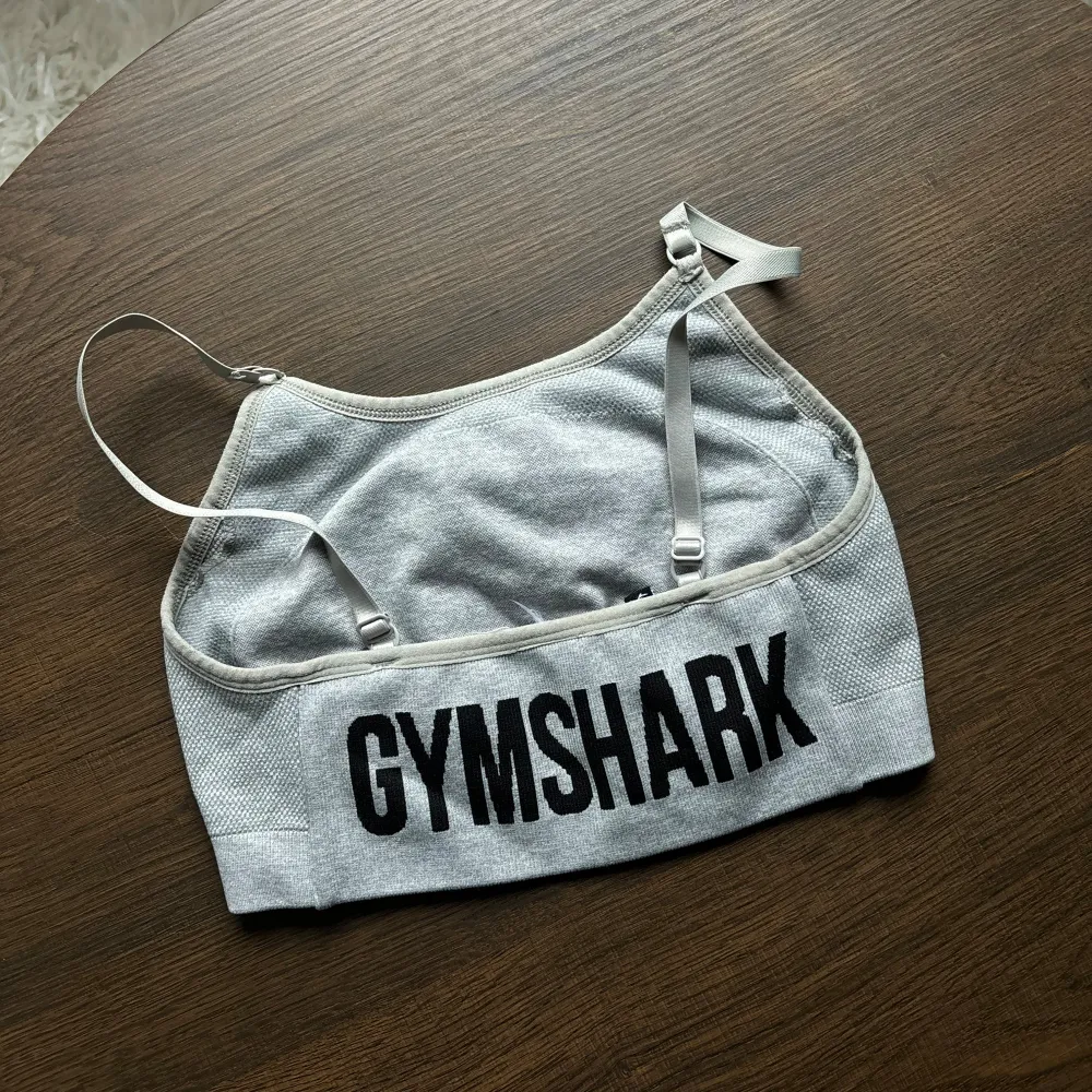 Säljer en grå sporttopp från Gymshark i mycket bra skick. Den är ärmlös med justerbara axelband och har en bekväm passform. Perfekt för träning eller vardagsbruk. Gymshark-loggan syns både fram och bak.. Sportswear.