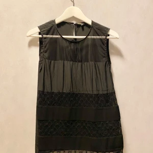 Svart ärmlös klänning med spetsdetaljer från Maje Paris - Snygg svart ärmlös klänning med transparenta meshdetaljer upptill och vackra spetsinslag. Perfekt för en festlig kväll! Klänningen har en rak passform, ej åtsittande, och är gjord i ett lätt och bekvämt material. Franska storlek 1 är samma 36 i Sverige. Märke: Maje (Paris). Oanvänd. 