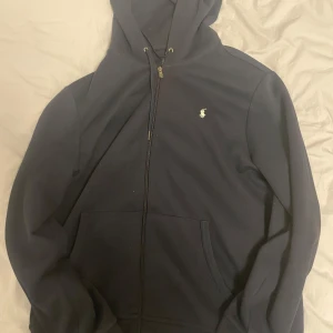 Svart hoodie från Ralph Lauren - Säljer en snygg mörkblå hoodie från Ralph Lauren i storlek L. Den har en dragkedja framtill och den klassiska loggan på bröstet. Mycket bra pris