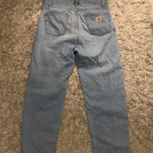 Säljer ett par ljusblå Carhartt jeans i modellen Landon Pant. De är i bra skick och har en avslappnad passform. Perfekta för vardagsbruk med en klassisk look. Tillverkade i 100% bomull för en bekväm känsla. Passar bra till både sneakers och kängor.