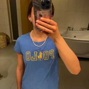 Blå t-shirt från Polo Ralph Lauren - Säljer en blå t-shirt från Polo Ralph Lauren i bra skick. Den har ett gult tryck med märkesloggan på framsidan. Perfekt för en avslappnad stil eller vardagsbruk. Kortärmad och bekväm passform. Säljes då den inte passar längre dp den är i storlek 152-164!