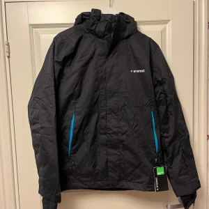 Helt ny Everest jacka - Svart jacka med huva i stl M. Jackan har en dragkedja framtill och två fickor på sidorna även en ficka på ärmen som inte är så synlig och en innerficka. Den är i toppenskick då den är helt ny med lapp på. Perfekt till vintern då den är väldigt varm.