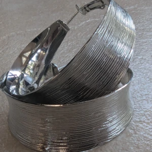 Stora silverfärgade örhängen -  Ett par stora, silverfärgade örhängen med en unik, vågig design. De har en texturerad yta som ger en cool och modern look. Perfekta för att piffa upp vilken outfit som helst. Lätta att bära och stängs med en enkel låsmekanism.aldrig använt.ny