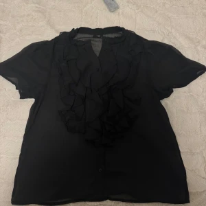 Topp/blus - En oanvänd blustopp med volanger, den är rätt så gebomskilning men jätte fin på då volangerna täcker brösten. Köpt för 499kr men säljer den för 300 då den är oanvänd, priset kan diskuteras och märket på tröjan är JDY. frakten ingår