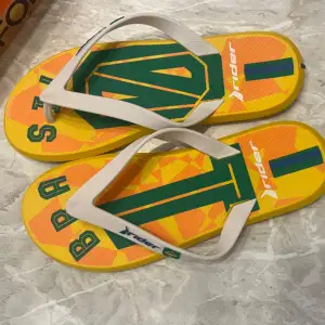 Säljer ett par supercoola flip-flops från Rider med Brasilien-tema. De har en färgglad design i gult, grönt och orange med texten 'Brasil' på sulan. Perfekta för sommaren och strandhäng! De är i nyskick aldrig använda. 🏖️ strl 43