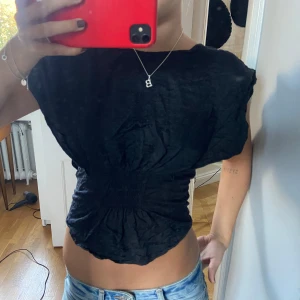 Svart topp med öppen rygg - Säljer en snygg svart topp med en cool öppen ryggdetalj. Toppen har en tight passform med smock i midjan . Perfekt för en utekväll eller fest! 💃