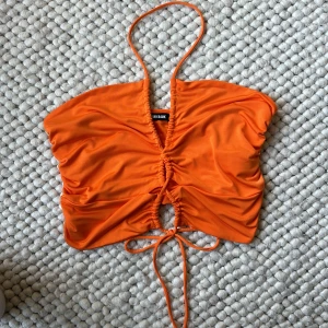 Orange topp från BikBok - Säljer en superfin orange topp från BikBok i storlek M. Den har en snygg snörning framtill och är gjord i ett mjukt och stretchigt material. Perfekt för sommardagar eller en festkväll! 💥