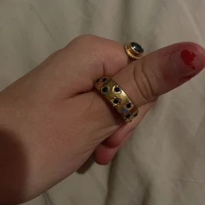 Guldring med färgade stenar - Säljer en snygg guldring med flera små färgade stenar i blått och grönt. Ringen har en bred design och ger en lyxig känsla. Perfekt för att piffa upp vilken outfit som helst! 💍✨