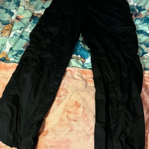 Svarta cargobyxor från Divided - Säljer ett par svarta cargobyxor från Divided. De har en loose passform och är perfekta för en avslappnad stil. Byxorna har flera praktiska fickor och är gjorda i ett slitstarkt material. Perfekta för höst och vår!