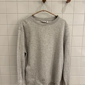 Grå sweatshirt från Weekday - Säljer en stilren och bekväm grå sweatshirt från Weekday. Perfekt för både vardag och mysiga hemmakvällar. Tröjan har en klassisk rund halsringning. Den är i bra skick och passar perfekt till jeans eller leggings. Hör av dig vid intresse!