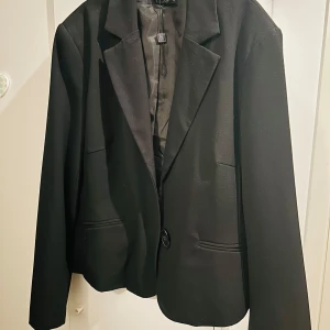 Svart kavaj från b.young - Snygg svart kavaj från b.young i storlek 42. Perfekt för både jobb och fest! Den har en klassisk design med knapp framtill och långa ärmar. Materialet känns bekvämt och stilrent. Ett måste i garderoben för en stilren look.