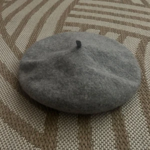 Grå ullbasker - Säljer en stilren och klassisk grå beret i ull. Perfekt för höst och vinter, den håller dig varm och ser chic ut samtidigt. Baskern har en liten topp i mitten. 