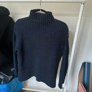 Stickad tröja  - Jättefin tröja från COS som är i en superfin marinblå färg, använd 1 gång. Tjockt material och med glitter på. Kragen går lite upp på halsen. 