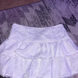 Vit volangkjol från Shein - Säljer en superfin vit volangkjol från Shein. Kjolen har ett  somrigt utseende med flera lager av volanger och ett diskret broderat mönster. Perfekt för sommarens alla fester eller en dag på stan. Den är i storlek XL och är i nyskick. 