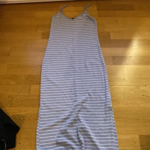 Klänning - Lång ljusblå klänning med tunna axelband, vita ränder och liten sprund i bak. 