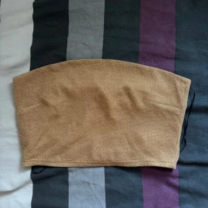 Guldig tubtopp från H&M - Säljer en snygg guldig tubtopp från H&M. Perfekt för festliga tillfällen med sin glittriga yta. Toppen är axelbandslös och har en tight passform. Superfin att matcha med både kjol och byxor för en glam look!