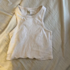 Vit ribbad linnetopp i storlek XS - Säljer en superfin vit ribbad linnetopp i storlek XS. Perfekt för sommardagar eller som ett basplagg i garderoben. Toppen är ärmlös och har en tight passform som framhäver figuren. Den är i nyskick och redo för nya äventyr!