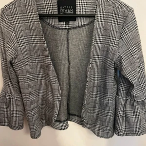 Trendig kort rutig kappa  - Trendig kort rutig kappa med ett stilrent mönster som lyfter vilken outfit som helst. Perfekt för både vardag och mer uppklädda tillfällen. Kappan är i ett bekvämt material och har en flatterande passform som når strax över höfterna. 