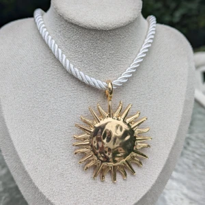 Guldigt solhalsband med vit snodd/ 1st Vintage rep Solroshänge Halsband, Charm Choker  - Unikt halsband med en stor, guldig solberlock. Berlocken har en cool, hamrad yta som ger den en extra dimension. Halsbandet har en tjock vit snodd som ger en snygg kontrast till den guldiga solen. Ny
