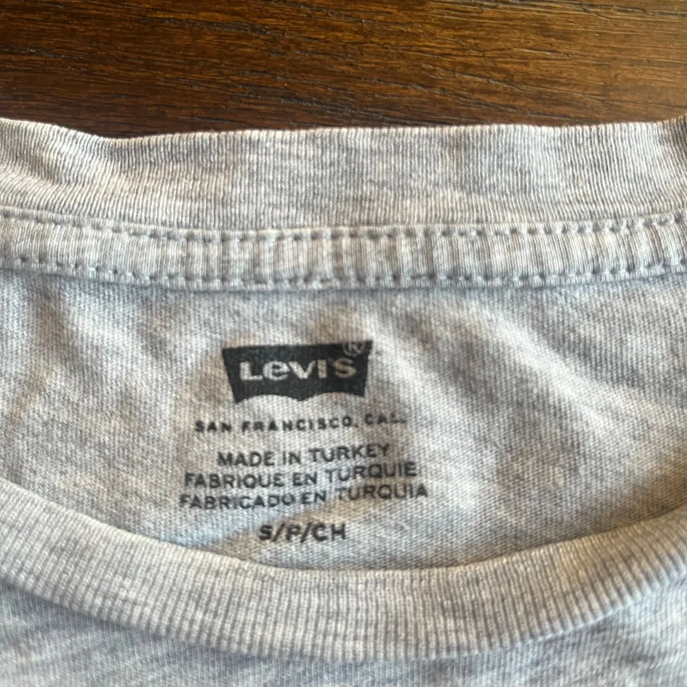 Säljer en grå t-shirt från Levi's i storlek S. Den har en klassisk design med det ikoniska Levi's-logotypen i rött och vitt på bröstet. Perfekt för en avslappnad stil och passar till det mesta. T-shirten är i bomull och har korta ärmar. ❤️. T-shirts.