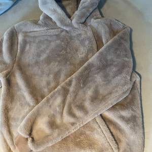 Supermjuk och gosig beige hoodie i fleece. Perfekt för kyliga dagar när du vill känna dig som en nallebjörn. Den har en stor huva och långa ärmar, vilket gör den extra mysig. Passar perfekt för höst och vinter. (Ny med prislappen på) 