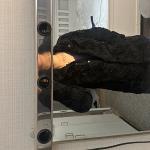 Svart pälsjacka från Vero Moda - Säljer en supermjuk och fluffig svart pälsjacka från Vero Moda. Den är perfekt för kyliga dagar och har en stilren design med knappar framtill. Jackan är långärmad och i nyskick, så den är redo att hålla dig varm och snygg hela vintern!