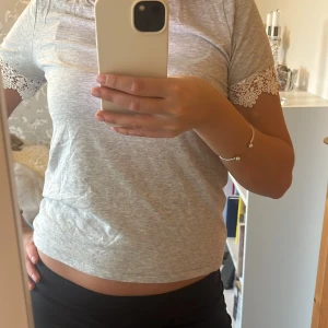 Grå t-shirt med spetsdetaljer - Säljer en grå t-shirt med korta ärmar och fina spetsdetaljer på armarna.