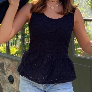 Svart ärmlös topp - Snygg svart ärmlös topp med broderade detaljer och peplumdesign. Perfekt för varma sommardagar eller en kväll ute. Kombinera med jeans eller kjol för en stilren look.