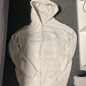 Vit hoodie med dragkedja och paljettdetaljer - Snygg vit hoodie med dragkedja och glittrande paljettdetaljer på bröstet. Ny skick, storlek M